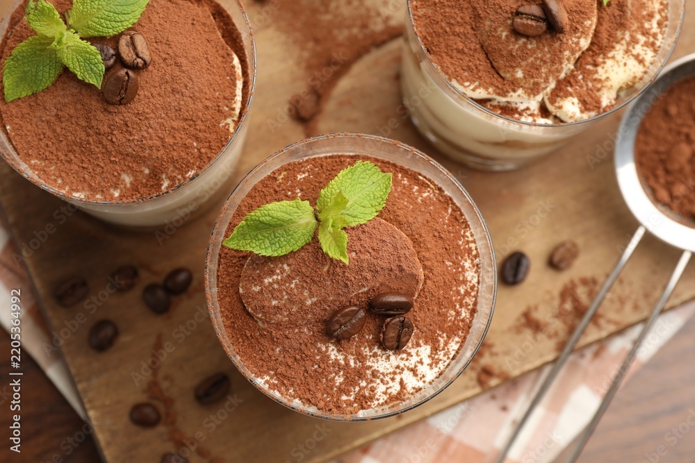 Fototapeta premium Tasty tiramisu with coffee beans and mint in glasses served on wooden table, flat lay