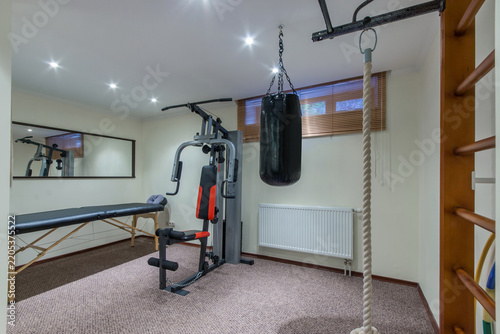 Bild auf Leinwand A small home gym features a multi-gym machine, a boxing bag, and a stretching rope