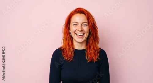 Portrait of a happy red-haired young woman laughing sincerely and cheerfully on a pink background
