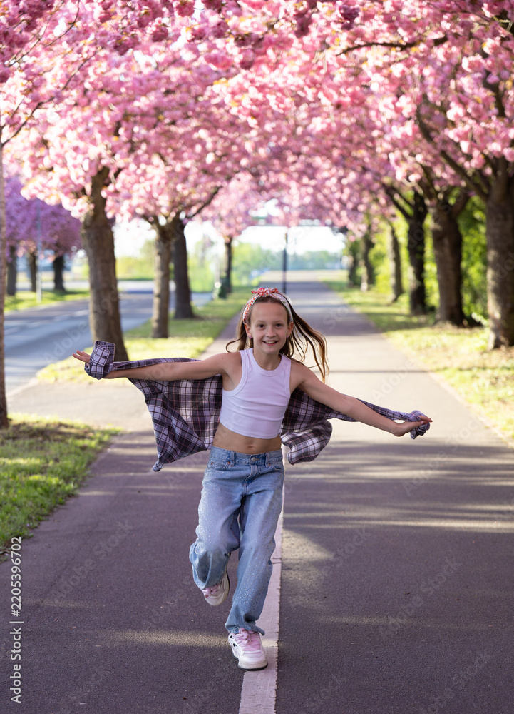 Obraz premium Playful girl running with shirt under blooming cherry blossom trees in spring park