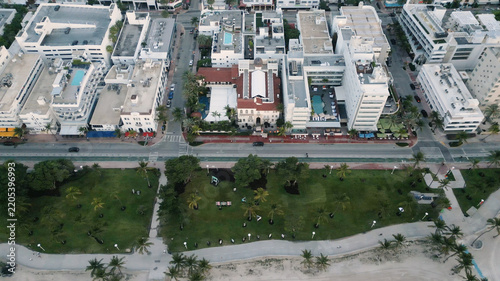 Aerial view of Miami Beach featuring lush palm trees in the park, coastal walkways, and urban architecture with hotels along the oceanfront in Miami Beach, Florida, United States.