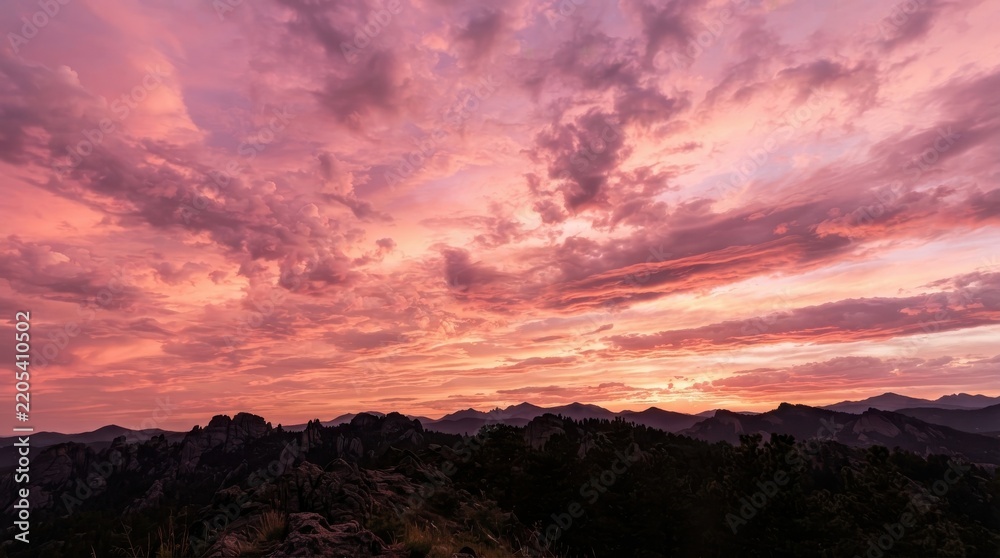 Fototapeta premium Vibrant pink and orange sunset sky over a dark mountainous horizon