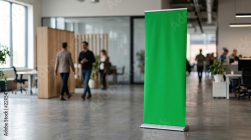 Vertical green retractable roll up banner stand placed on concrete office floor for corporate event trade show presentation.