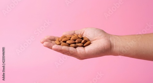 A handful of organic raw almonds held in an open palm against a vibrant pink background, representing a healthy snack, nutritious diet, vegan protein, and a wellness-oriented lifestyle.