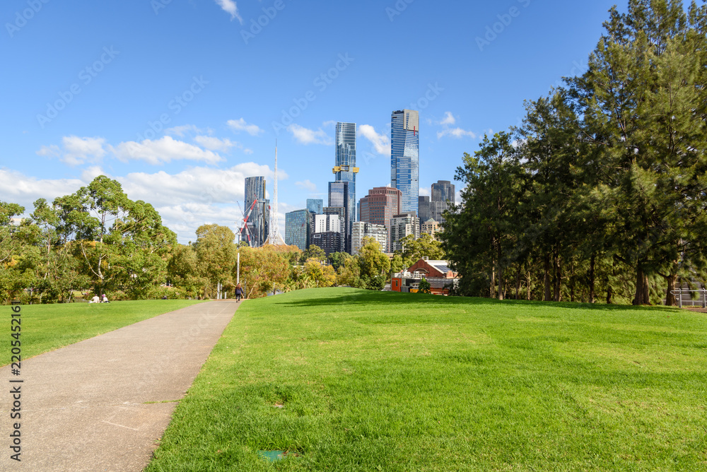 Naklejka premium Paved footpath running between lawns in a public park in a city centre on a sunny autumn day. Modern high rise residential and office buildings are visible in background.