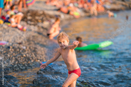 Blond boy playing on a crowded rocky beach in golden evening light.