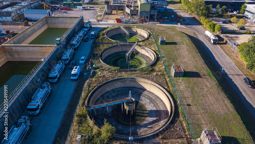 Aerial view of the sewage works in Camberley, showing circular sedimentation tanks, industrial infrastructure, and a line of tanker trucks parked nearby in Camberley, England, United Kingdom.