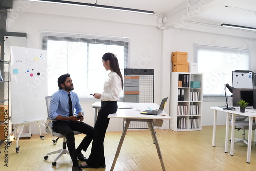 Fotografie Wide shot of young Indian businessman and Asian businesswoman, candid workplace