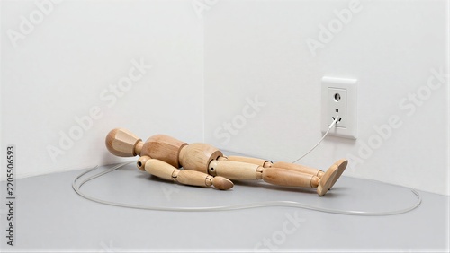Wooden mannequin lies on floor, plugged into wall socket as if charging.