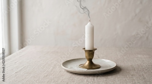 White candle releases a wispy trail of smoke after being extinguished on a brass holder.