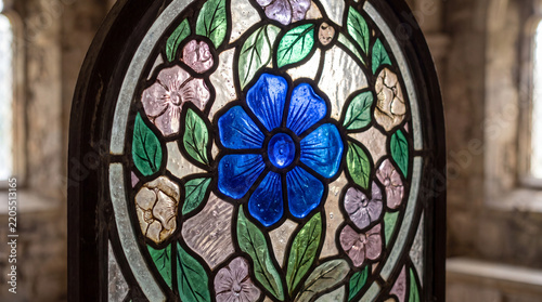 A detailed close-up of a circular stained glass window featuring a prominent blue flower surrounded by pink blossoms and green leaves in a historic building.