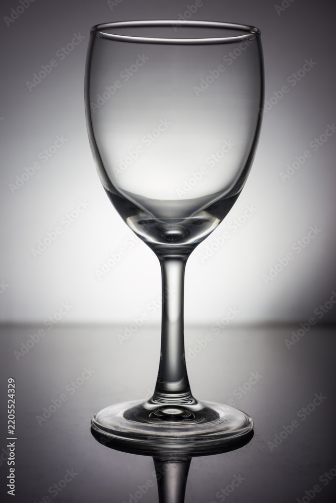 Obraz premium A clean, empty transparent wine glass placed on a smooth reflective surface in a studio setting, captured in monochrome tones.