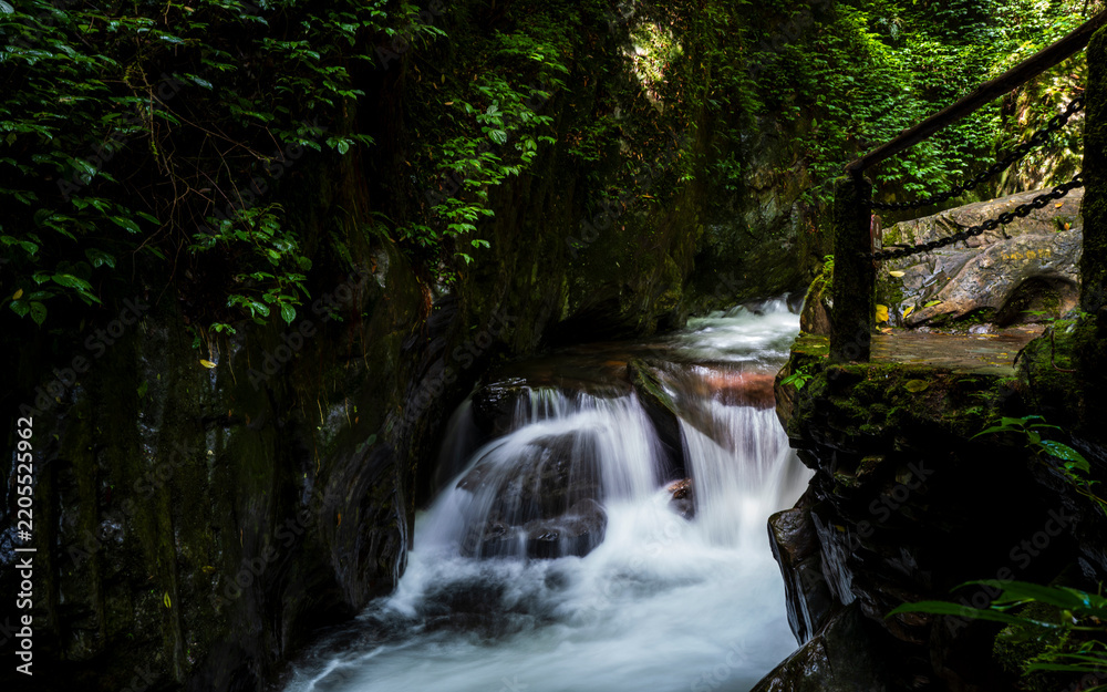 Fototapeta premium Slow motion stream among wet rocks in Shimen Gorge, Ailao Mountain, Yuxi, Yunnan, China. Forest creek flowing over mossy stones, long exposure photography.