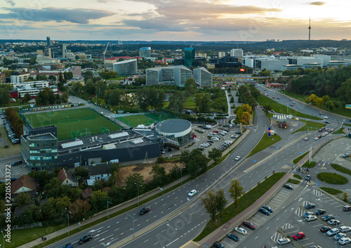 Aerial view of the city of Vilnius featuring modern office buildings, a sports field, and urban roads during the golden hour in Vilnius, Vilnius County, Lithuania.