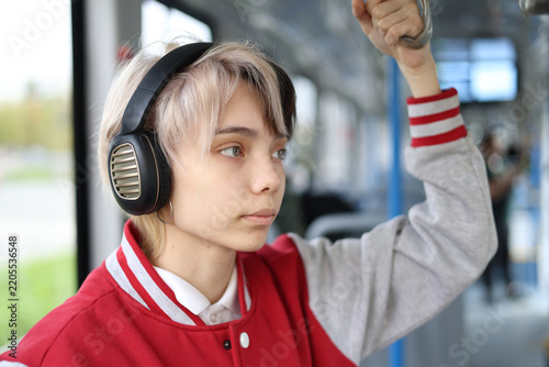 Close up of a teenage girl rides a city tram she standing and listening to music through headphones.