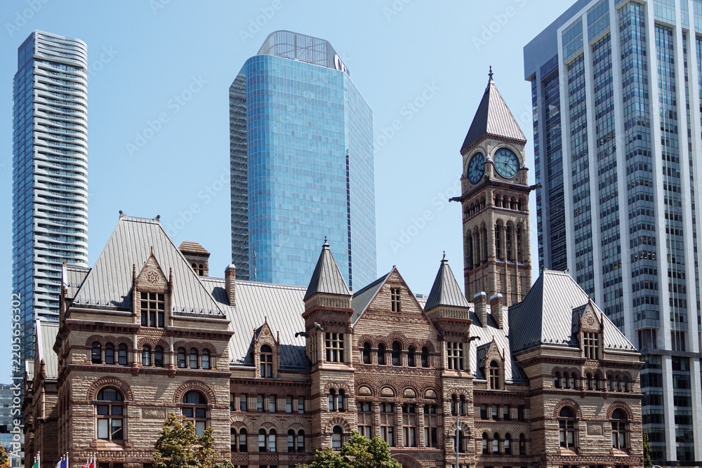 Obraz premium Historic Old City Hall clock tower framed by modern skyscrapers in downtown Toronto on a bright clear day. g.