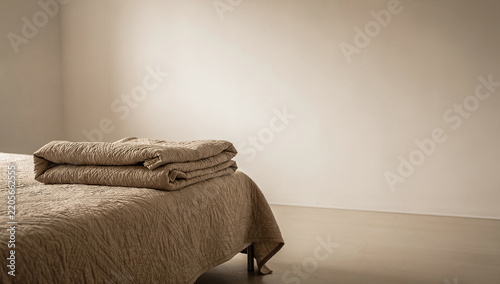 A folded beige quilted bedspread and coverlet on a bed in a minimalist neutral bedroom interior