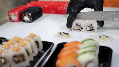 Close-up of a chef wearing gloves slicing a variety of sushi in a restaurant kitchen. There are many plates with different types of sushi on the table. Japanese restaurant. The concept of catering.