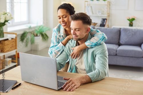 Happy young mixed race at home office workplace using laptop computer for remote work, searching for information, giving each other advice, building relationship with mutual trust and support