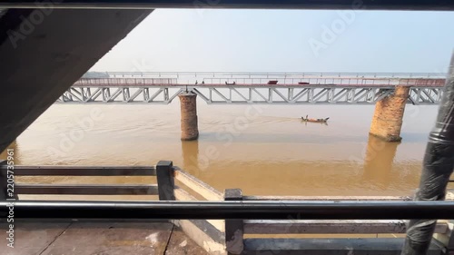 View of Historic Old Godavari Havelock Bridge and Stone Piers Seen from Moving Train. Small Wooden Fishing Boat Sailing Under Historic Railway Bridge Across Wide Godavari River.
