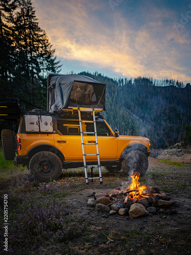 Yellow overland vehicle with tent parked by a campfire