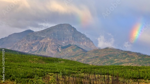 Rainbow and clouds over a mountain peak and green forest