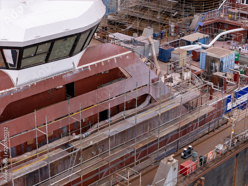 Aerial view of a ship under construction in a shipyard featuring extensive scaffolding around the metal hull and the bridge structure in Gdansk, Poland.