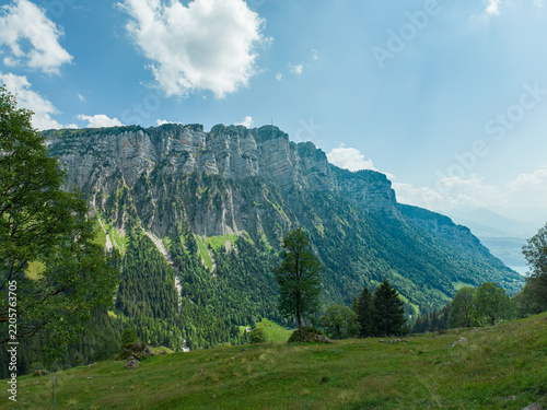 Aerial view of the Justistal valley and the Niederhorn mountain range with lush green slopes, dense forests, and a glimpse of Lake Thun in Sigriswil, Bern, Switzerland.