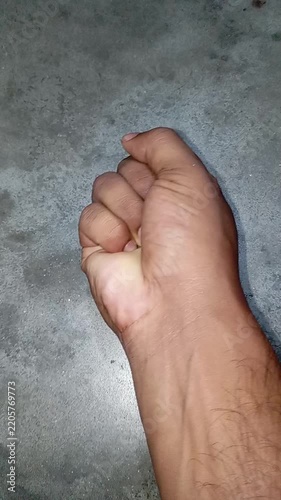 Close up of a male hand repeatedly clenching into a tight fist against a grey background