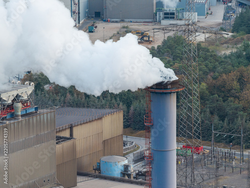 Aerial view of the industrial manufacturing facility at Genk-Zuid Rechteroever with a tall chimney emitting smoke, surrounded by industrial infrastructure in Genk, Vlaanderen, Belgium.