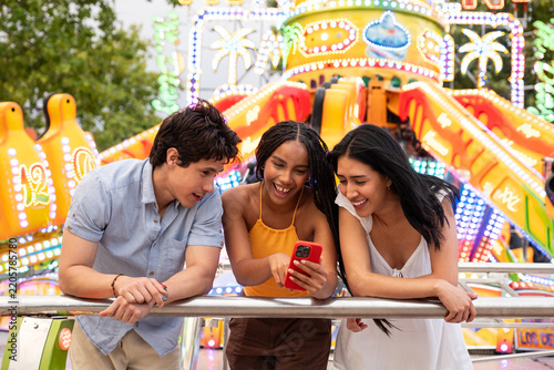 Diverse friends sharing a laugh while watching content on a smartphone at a fair