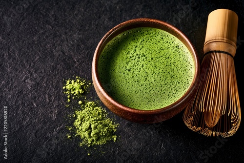 Matcha green tea bowl with bamboo whisk and powder on dark stone surface in a moody overhead macro shot for wellness branding and health cafe marketing