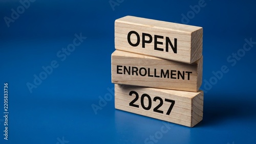 Open enrollment 2027 concept on stacked wooden blocks, health insurance plan registration typography on wooden cubes, educational application concept against blue background