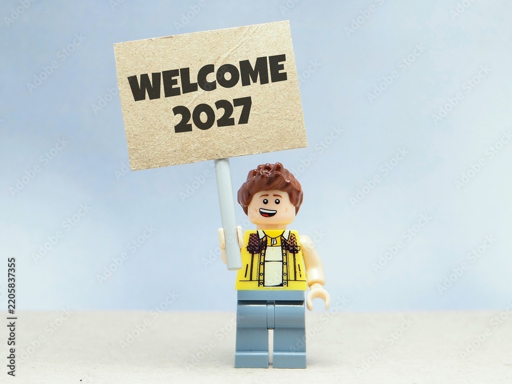 Obraz premium Indonesia - June 12, 2026 : Mini toy of action figure at table with blurred background. Miniature photography concept design. Minifigure of people with HAPPY NEW YEAR 2027 text at poster banner.