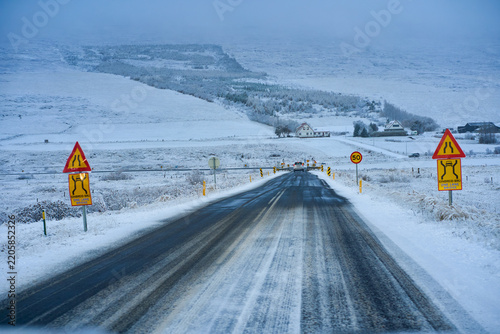 Driver's view of an icy snow-covered road trip in Iceland during winter with road signs and one-lane bridge. Scenic rural arctic driving experience.