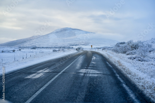 Driver point of view along icy asphalt road leading toward scenic snow-covered mountain in Iceland winter. Arctic highway road trip and travel adventure.