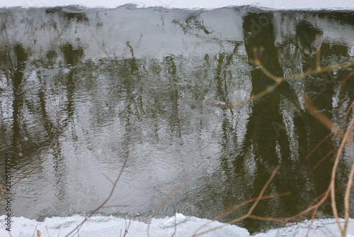Fotografie The dark river surface reflects silhouettes of snow covered trees in winter forest