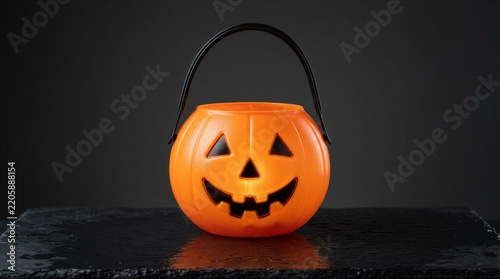 Bright orange plastic pumpkin candy bucket for trick or treat on a dark slate background