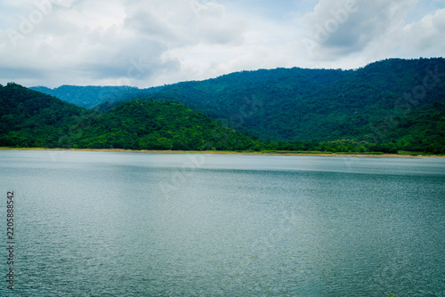 Scenic river reflection with green mountains under a cloudy blue sky.