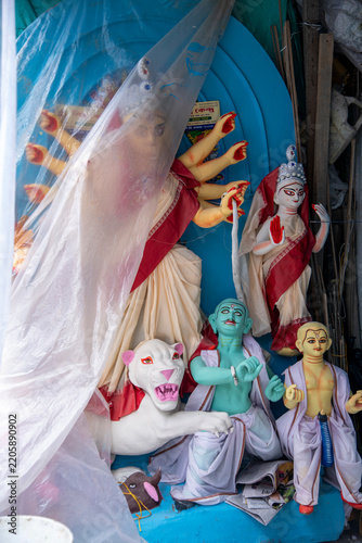 A vibrant, partially completed clay sculpture of Goddess Durga stands inside a traditional clay-modeling workshop in Kumartuli, Kolkata. The colorful idol is partially draped in a plastic cover 