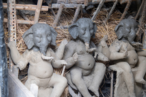 An authentic behind-the-scenes view inside a traditional artisan workshop in Kumartuli, Kolkata, featuring three unfinished clay idols of Lord Ganesha in various stages of sculpting.