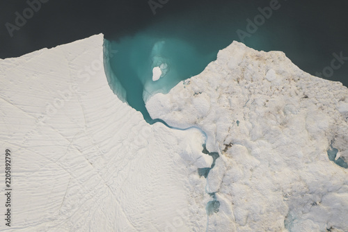 Aerial view of a massive iceberg floating in the turquoise waters of the Ilulissat Icefjord, showcasing intricate ice textures and deep crevasses Ilulissat, Avannaata Municipalit, Greenland.