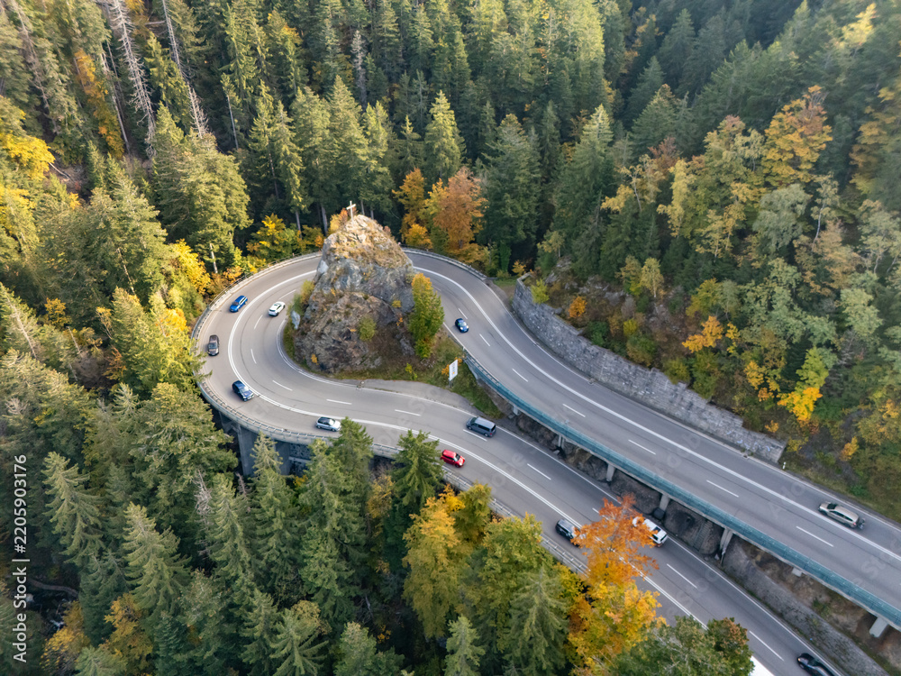Naklejka premium Aerial view of a hairpin mountain road curve with a cross on rock in autumn