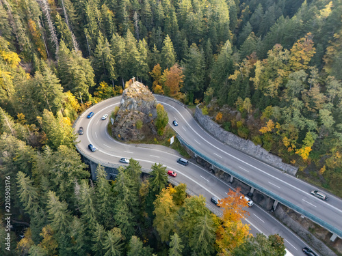 Aerial view of a hairpin mountain road curve with a cross on rock in autumn