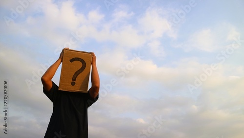 Person wearing a cardboard box with a question mark over their head against a cloudy sky.