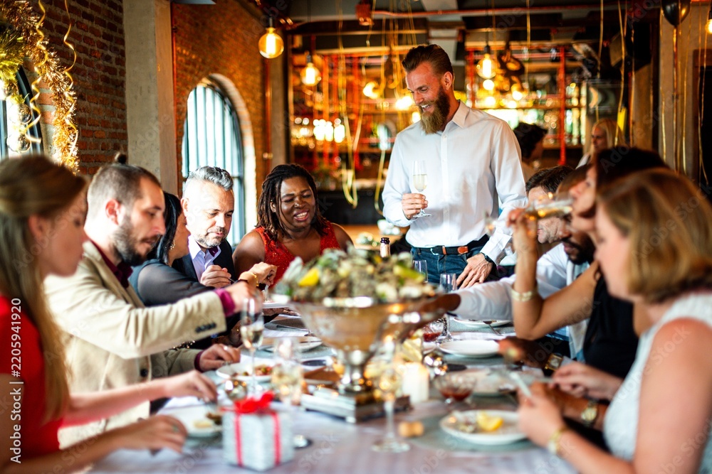 Obraz premium Diverse group enjoying a festive meal in a warmly lit restaurant setting.