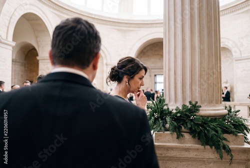 Elegant woman in evening dress listening attentively during a formal event or wedding inside a grand classical hall