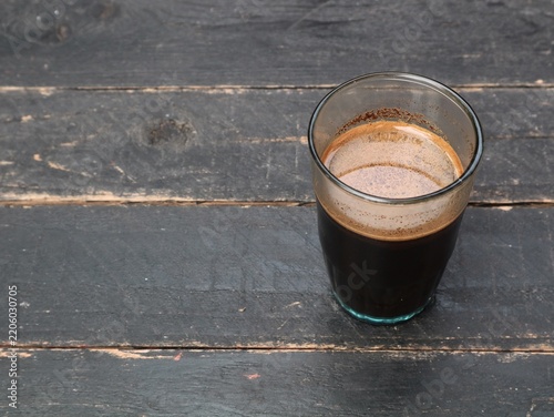 High angle view of a glass of hot black coffee on a rustic dark wooden table background. Morning energy drink, caffeine, cafe culture, and cozy breakfast concept photography with negative space