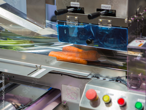 Fresh carrots and vegetables being packaged in plastic film wrap