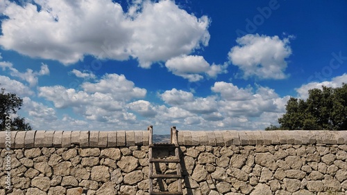 Old wooden ladder over a traditional dry stone wall under a blue cloudy sky.

